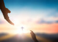 Help hand of God reaching over blurred cross on sunrise  background