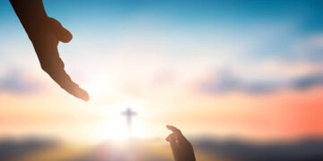 Help hand of God reaching over blurred cross on sunrise  background